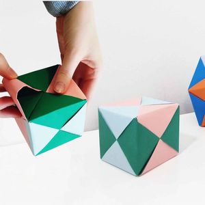 Kädet taittelevat värikästä origamikuuutiota, taustalla origamikuutio sekä tähtimäistetty oktaedri