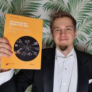 Juuso Autiosalo holding his doctoral dissertation.