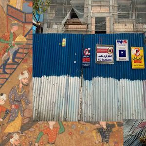 The Image is a collage made by Ali Mousavi. The image's background is a Persian miniature that depicts people engaged in various activities such as playing music, dancing, reading poetry and constructing their environment within a garden. A traditional way of life that seems to be developing according to historical and cultural values. In the foreground, there are two images from a contemporary housing construction/materials that are imposed on the traditional way of life that is diminishing.