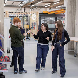 Four students talk in a workshop, surrounded by tools, workbenches and industrial equipment.