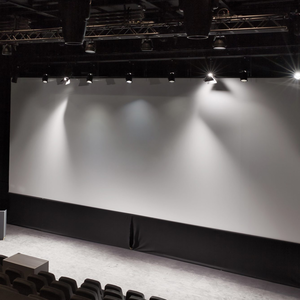 Empty dark auditorium with a wide white screen, spotlights above and rows of black seats in front; marsio cinema stage