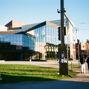 Modern glass-fronted building by a grassy street as three people walk past in bright daylight