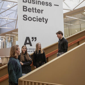 Neljä opiskelijaa juttelee sisäportaissa suuren Business–Better Society -kyltin vieressä aulassa