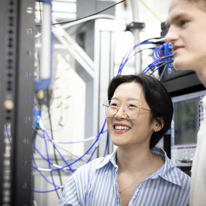 Two people smiling beside server racks with blue cables in a bright technical lab