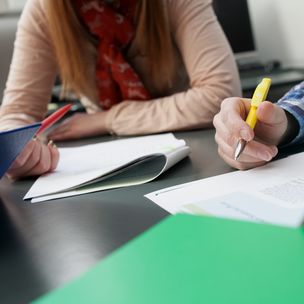 Close-up of two students making notes to research articles that they are reading.