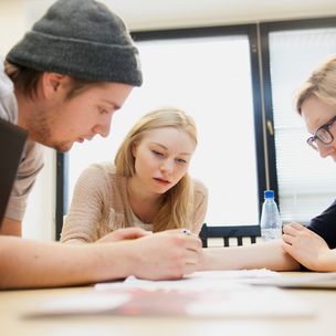 Three Aalto University students are doing group work by writing on paper together.