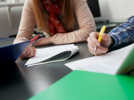 Close-up of two students making notes to research articles that they are reading.