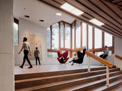Stairs landing in Dipoli with people sitting in two armchairs and looking at a painting / photo by Aalto University, Tuomas Uusheimo