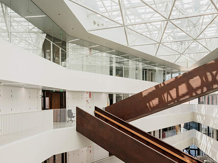 Väre building in the campus. Inside shot of natural light filled dark wood staircase criss-crossing in white surroundings. Light through skylights. Photo by Aalto University / Tuomas Uusheimo