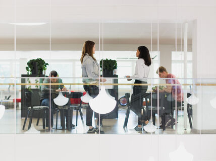 People talking and working in the café in Harald Herlin Learning Center, white lamps hanging in front.