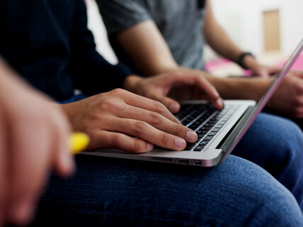 A man typing with a laptop on their lap. Only showing their arms and the laptop on their lap. Photo by Aalto University