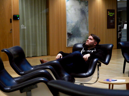 Jesse Rajala sitting in a big armchair in the Business School lobby, looking up. 