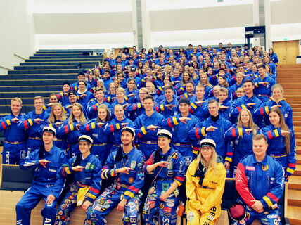 Image of lots of students wearing blue overalls and making a handsign for their guild