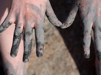 Hands covered in clay, orange henna tattoo showing on both hands