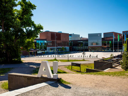 White A! logo standing on the ground with A-bloc and Väre in the background.