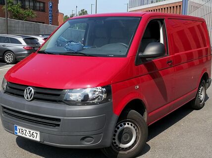 A red Volkswagen van is parked in a parking lot, with other cars and buildings in the background.