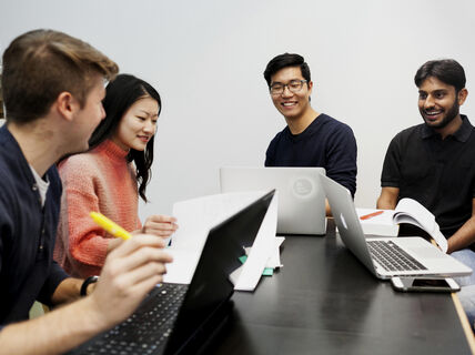 Four students studying together. Three of them have their computer and one is having papers in front of them.
