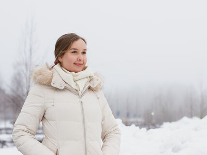 Heli Julkunen seisoo talvisessa maisemassa ja katsoo hymyillen pois kamerasta. Hänellä on päällään valkoinen talvitakki ja taustalla näkyy sumua, puita ja lumihankia.