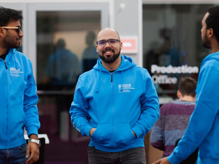 Henkilökuvassa hymyilevä, parrakas ja silmälasipäinen Bruno Duarte on kahden muun miehen kanssa. Heillä kaikilla on siniset SECCLO-tunnuksin varustetut hupparit päällään.