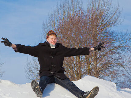 A happy student slides downhill a snowbank