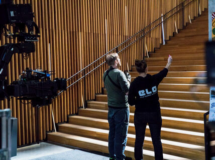 Kaksi elokuvantekijää keskustelee kohtauksesta puisen portaikon vieressä, vasemmalla kameravarusteita.