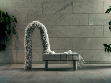 an organic shaped hairy sculptural object leaning against a table with smaller sculptures on it