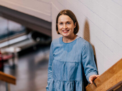 Professori Paula Jouhten nojaa kaiteeseen ja hymyilee kameralle.