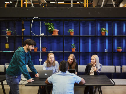 Students sitting around a table with laptops and discussing.