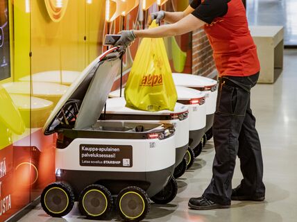 Nainen lastaa ostoksia kuljetusrobottiin Alepan edessä