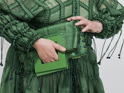 A hand holding green purse on top of a green dress