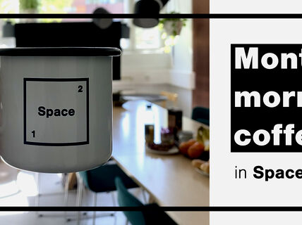 White coffee cup with Space 21 logo, space's common room on the background.