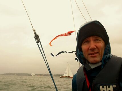 Huppupäinen mies purjeveneessä katsoo eteenpäin, sää on tuulinen  