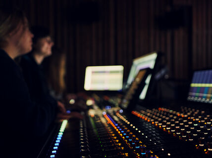 Two people seated next to an audio mixer