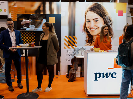Smiling people standing in front of a colorful wall with PwC logo 