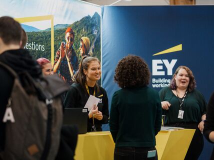 Smiling people standing and talking in front of a colorful wall with EY logo
