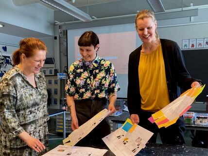 A teacher and two researchers smiling and sorting through paper presentations in a classroom