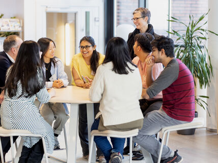 Smiling people sitting and standing around a table.