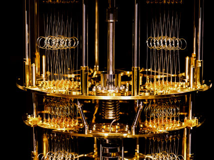 An illuminated gold-plated cryostat built by Bluefors sits on a black background.