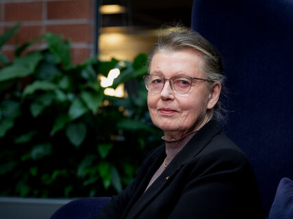 Professori Kaisa Nyberg istuu isolla tuolilla Aalto-yliopiston tietotekniikan talossa, tasutalla on viherkasveja