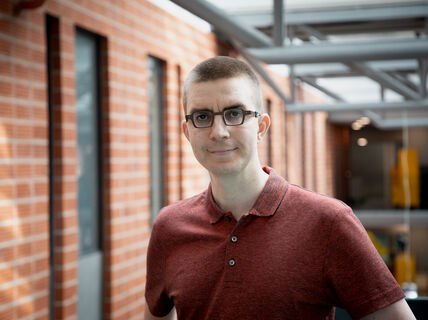 Associate Professor Jukka Suomela smiling at camera, dressed in a red shirt against a red-brick wall at the Department of Computer Science