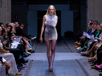 Malli kävelee yleisön reunustamalla catwalkilla kohti kameraa