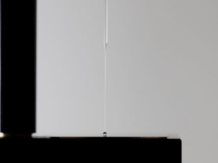 A glass needle probes a tiny droplet sitting on a black surface.