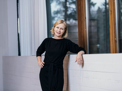 Woman in red dress leans against a light wall with windows