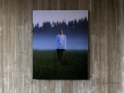 Valokuvateos naisesta ruohikolla, takana sumuinen metsä