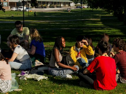 A group of Aalto University Summer School students sitting and chatting in the grass on Aalto campus.