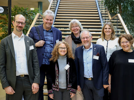 A group of people (SAB) wearing name badges standing in front of a staircase with plants around.