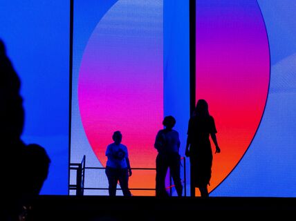 Silhouetted people stand before a large screen displaying a vibrant gradient from blue to pink and orange.
