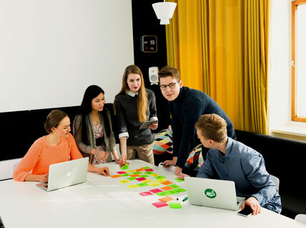 A group of people collaborate around a table covered with sticky notes and laptops in a modern office.