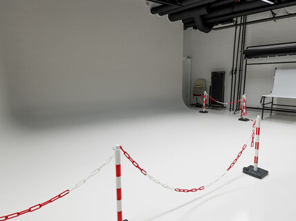 A photography studio with white walls and floor, bordered off with red and white chains.