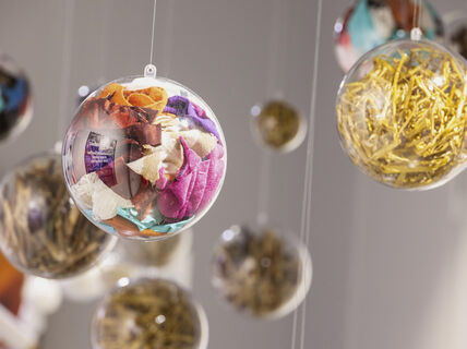 Läpinäkyvät pallot roikkuvat, täynnä värikkäitä kangastilkkuja ja kiiltäviä kultaisia esineitä.